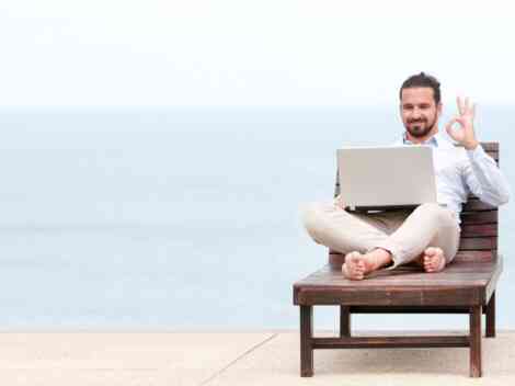 Small business owner working on a laptop by the beach, symbolizing the flexibility and freedom of hiring freelancers to scale business operations.