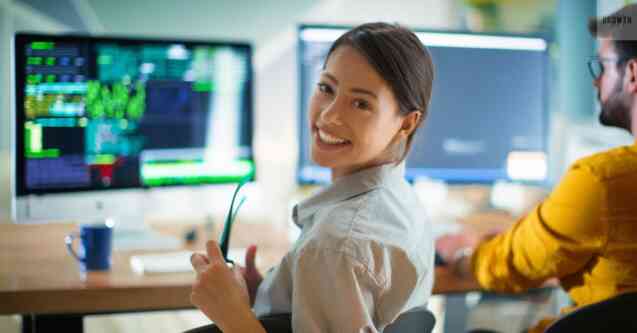 Woman smiling in front of computer screens, representing scaling your small business with project management tools and software.